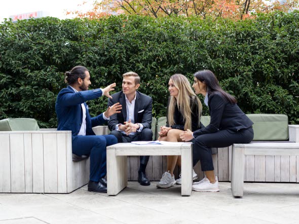 Fire personer sidder i samtale rundt om et bord uden for