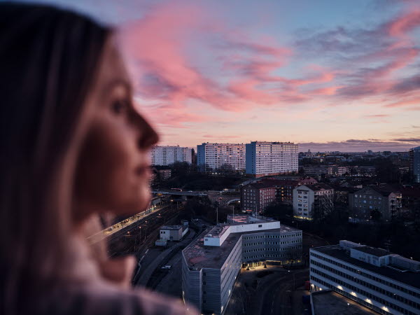 En kvinde ses fra siden med en udsigt over byen bag sig, mens hun kigger ud over byen og ser eftertænksom ud