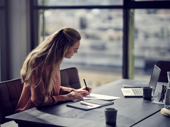 En kvinde sidder og skriver på et stykke papir ved et skrivebord