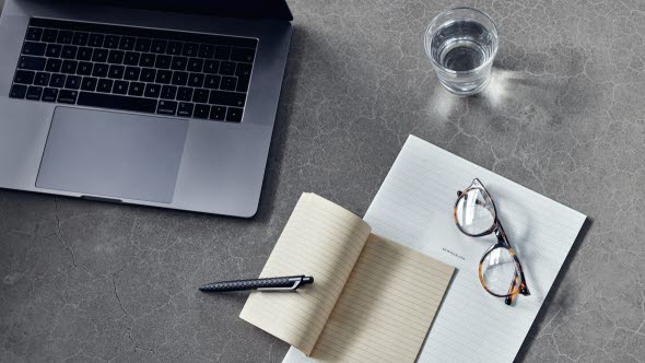 A desk with a laptop a notebook and glasses